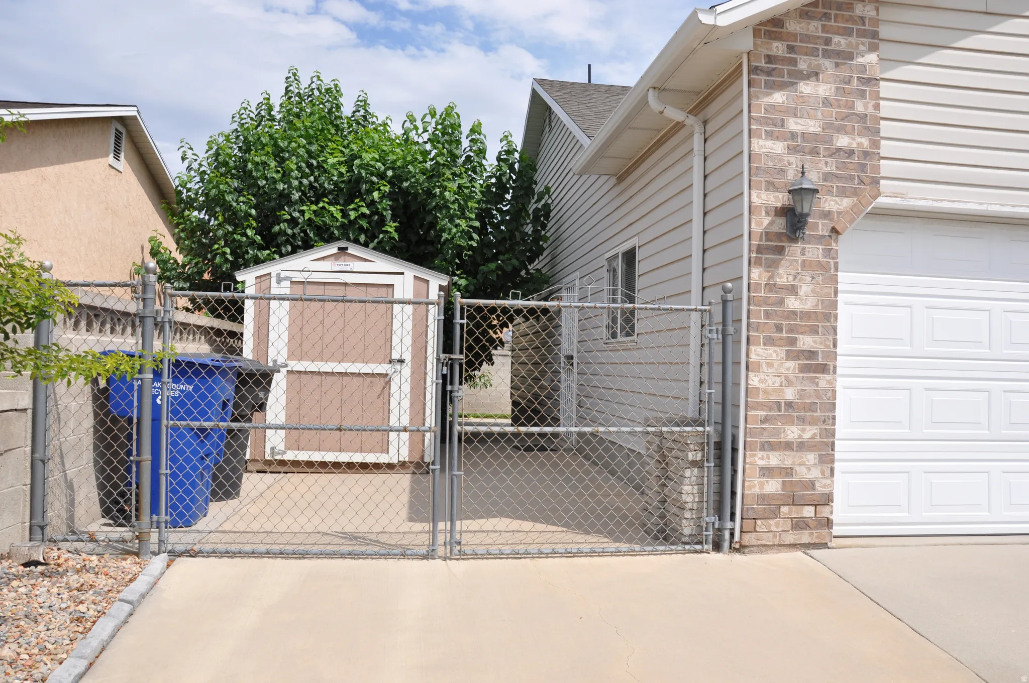 Chain link fencing with gate, concrete driveway, brick exterior accent, horizontal siding, and a detached storage shed