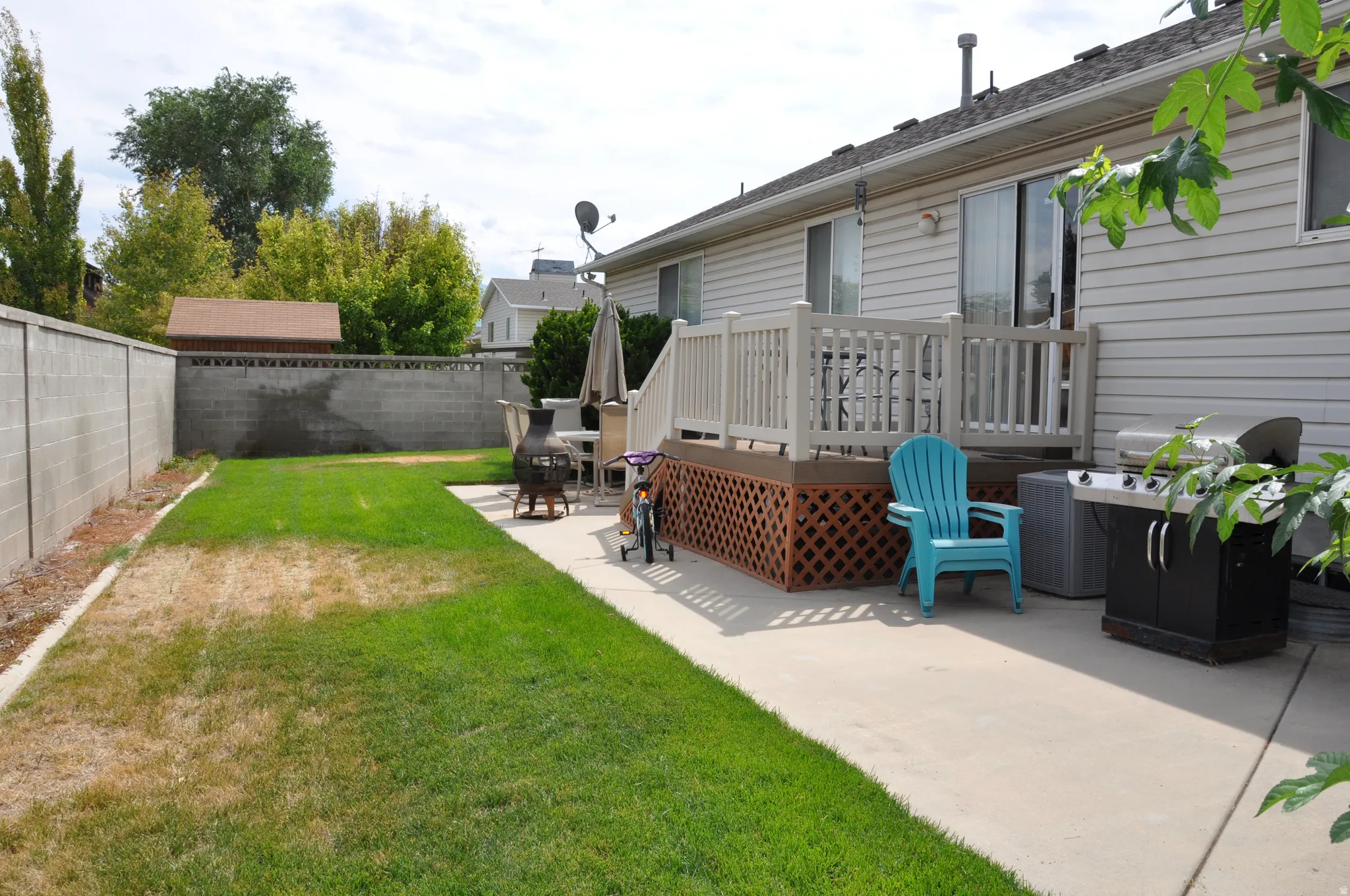Expansive backyard featuring a concrete patio, wood-finish deck with lattice skirting, and a concrete block perimeter fence