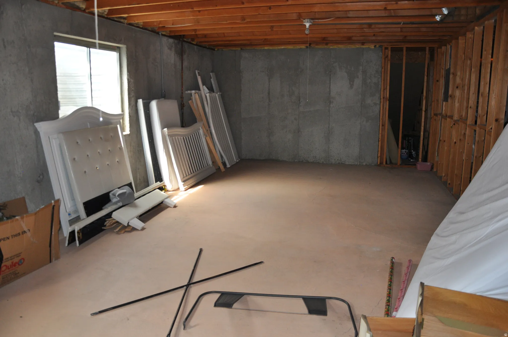 Unfinished space with exposed concrete walls, exposed wood ceiling joists, and a window for natural light