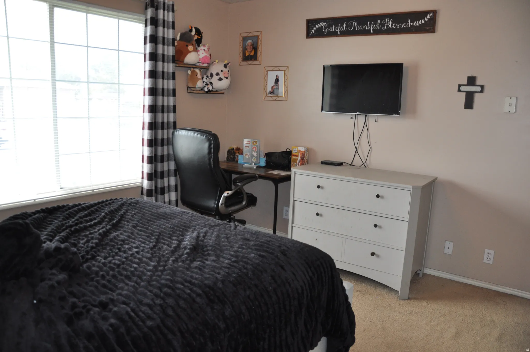 Wall-mounted television with visible wiring and a light-toned dresser featuring black knobs