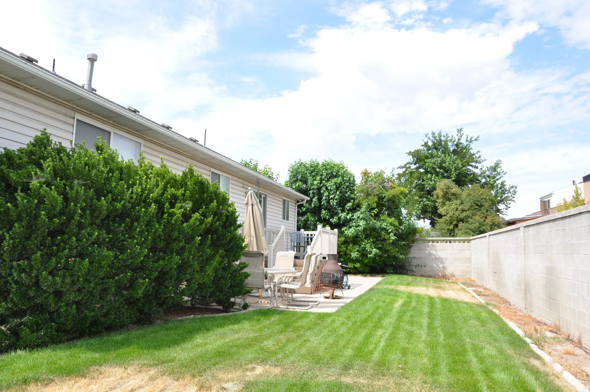 Expansive grassy yard with mature shrubbery, a concrete block privacy wall, and a concrete patio