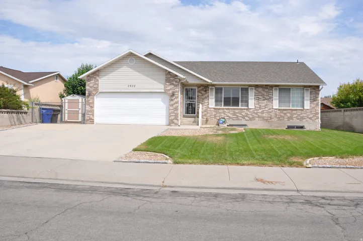 Brick and siding exterior, attached garage, concrete driveway, front lawn, and mature trees