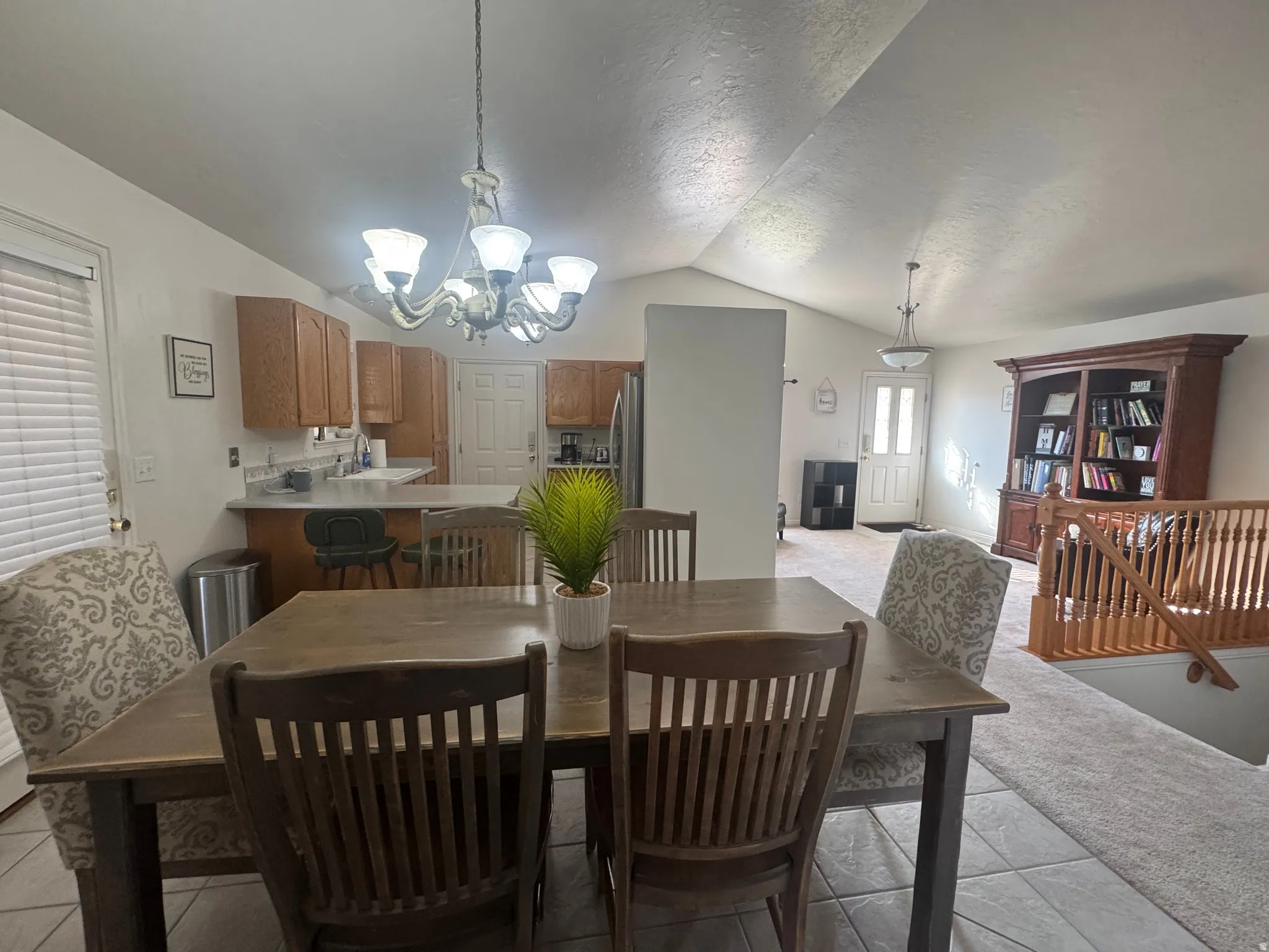 Vaulted ceilings with a five-light chandelier, wood-finish cabinetry, tile flooring, and a built-in bookcase