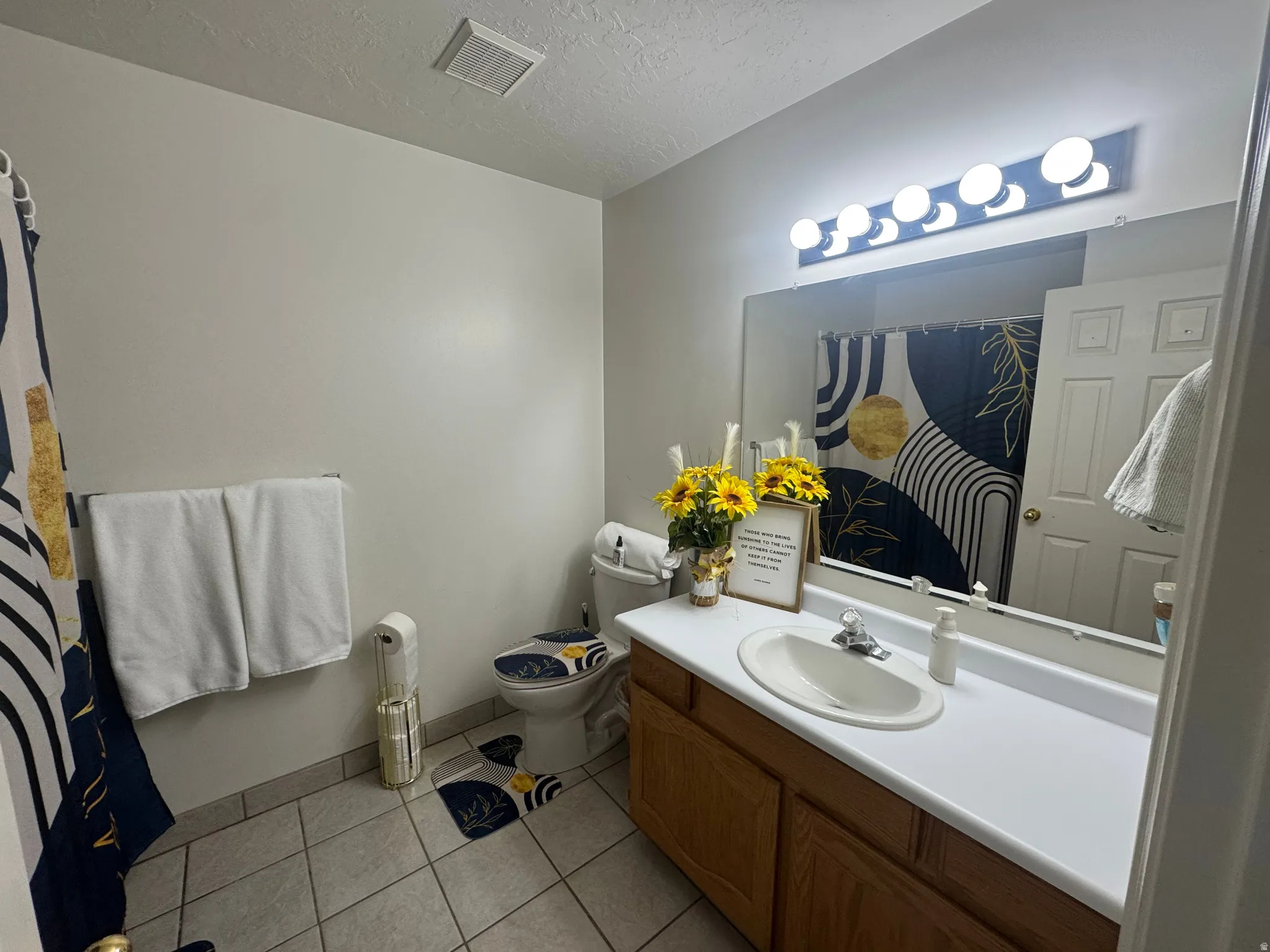 Bathroom featuring a single vanity with an integrated sink, wood-finish cabinetry, a large wall-mounted mirror, and tile flooring