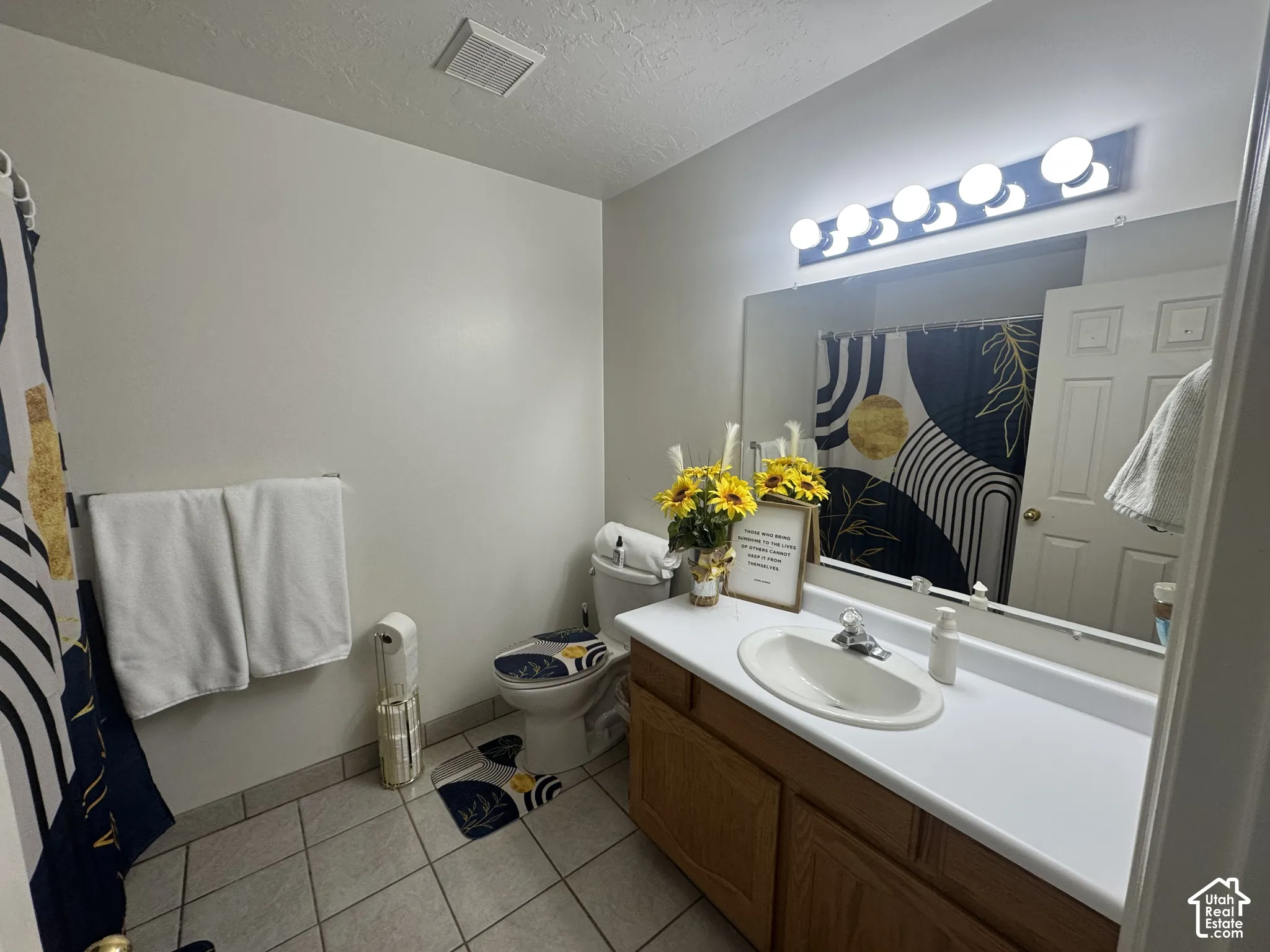 Full guest bathroom on main level features a single vanity with an integrated sink, wood-finish cabinetry, a large wall-mounted mirror, and tile flooring