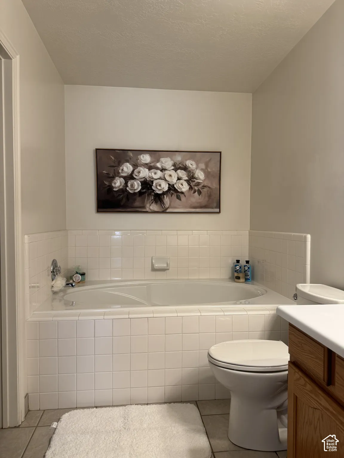 Built-in soaking tub with white tile surround, floor tile, and a toilet