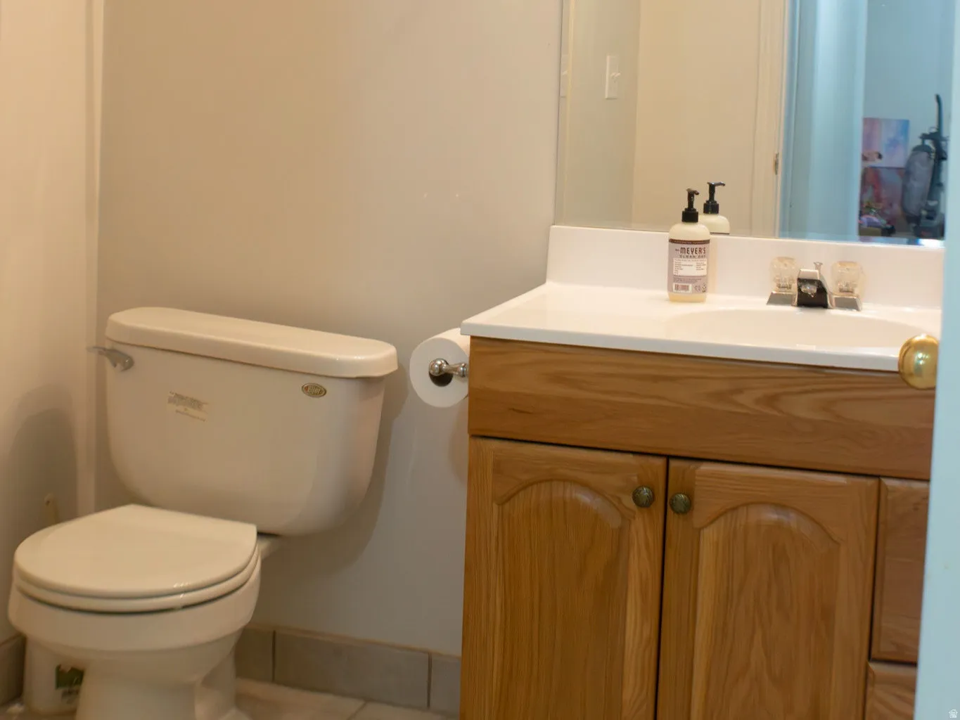 White vanity countertop with integrated sink, wood-finish cabinetry, and ceramic tile flooring