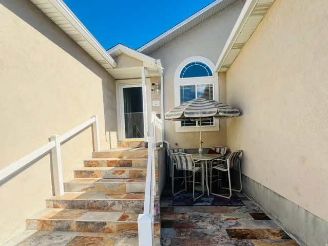 Stone tile patio with matching stairs, stucco exterior, arched window, and covered entry