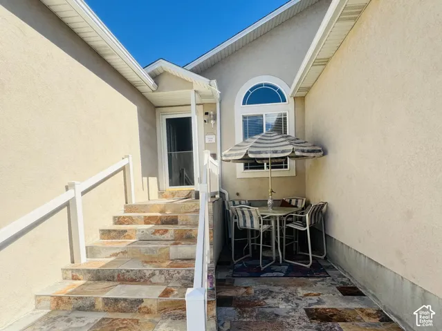 Stone tile patio with matching stairs, stucco exterior, arched window, and covered entry
