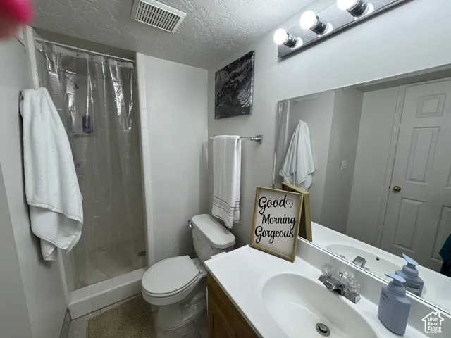 This bathroom featuring a shower stall, toilet, vanity with integrated sink, and an expansive wall-mounted mirror is conveniently located right next to the basement bedrooms.