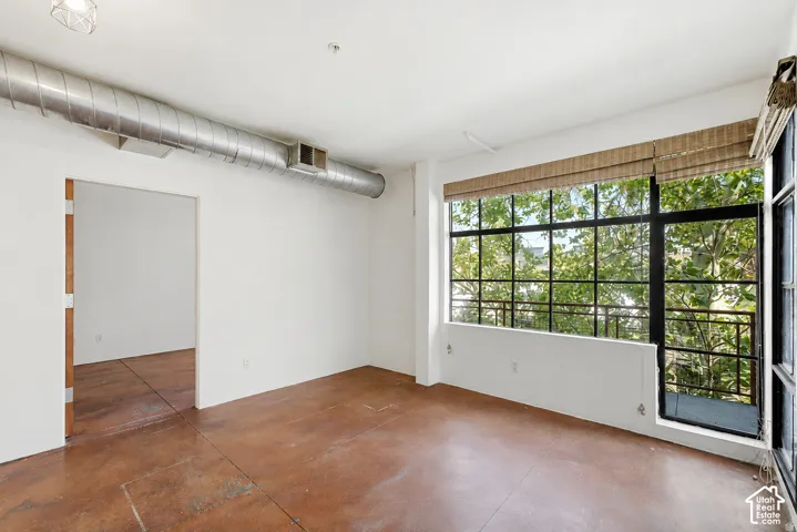 Expansive industrial-style windows, exposed metal ductwork, concrete flooring, and a balcony with metal railing