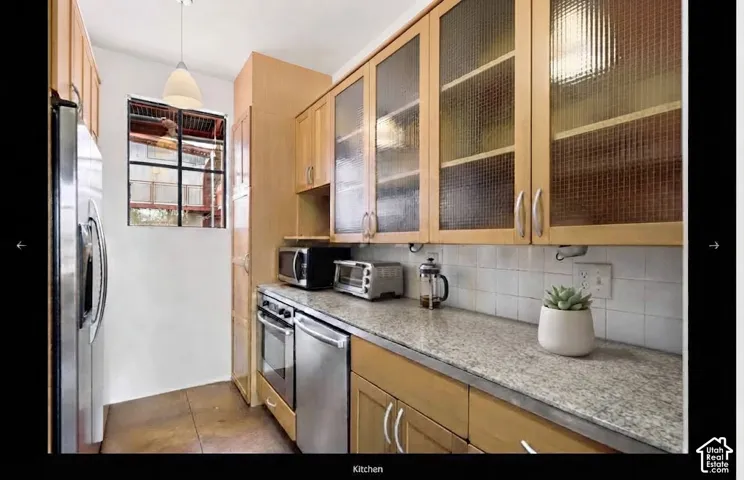 Kitchen with wood-finish cabinetry, patterned glass-front upper cabinets, stainless steel appliances, and a light-toned countertop
