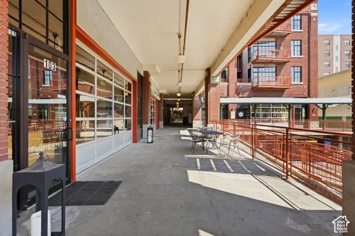 Covered outdoor walkway featuring concrete flooring, red brick walls, and multiple storefront entries with overhead glass panel doors