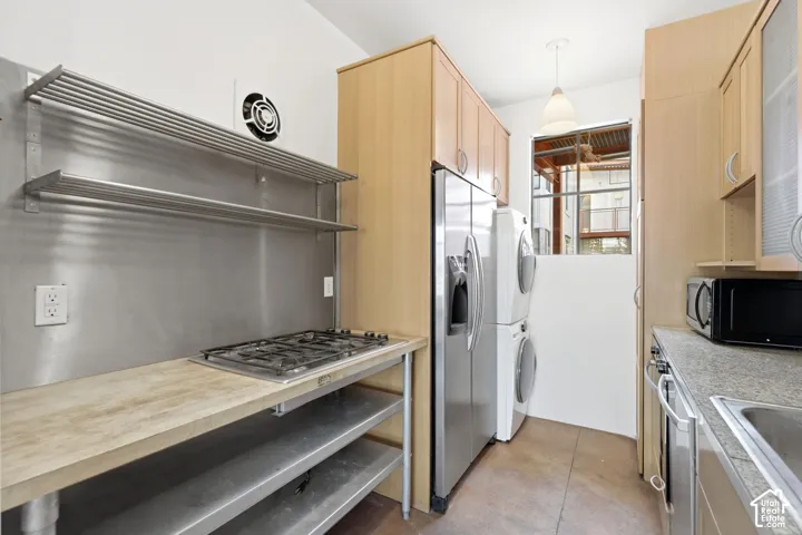 Stainless steel backsplash with integrated shelving, built-in gas range, wood-finish countertop, stacked washer and dryer, and upper cabinetry