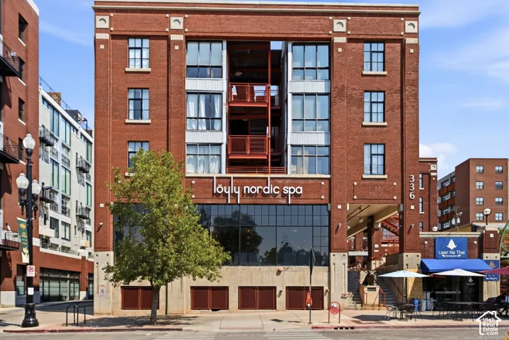 Red brick facade with large storefront windows, multi-level exterior balconies, and industrial-style windows