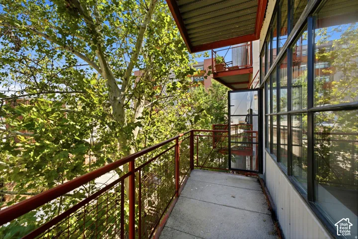 Balcony with concrete flooring, red metal railings, and a grid-patterned glass door