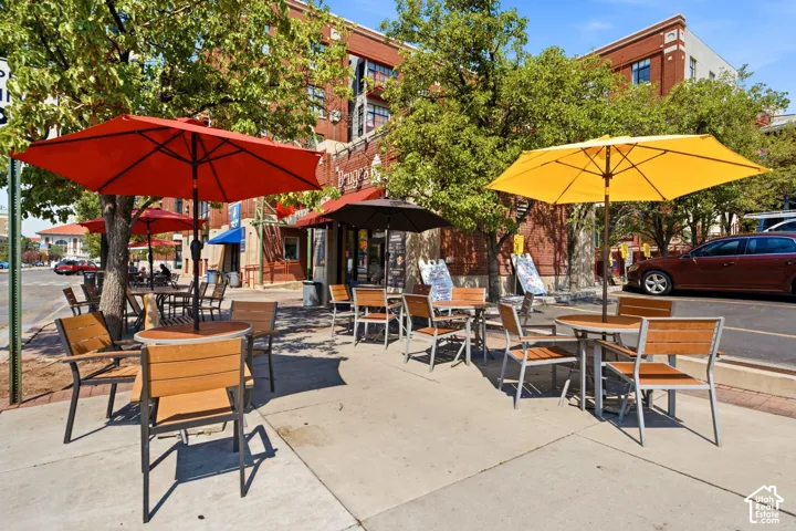 Street-level commercial space featuring brick facade, sidewalk dining area, and mature trees