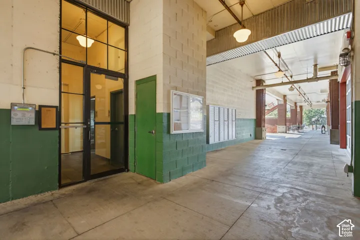 Covered concrete walkway with exposed corrugated metal ceiling, industrial-style lighting, and brick support columns