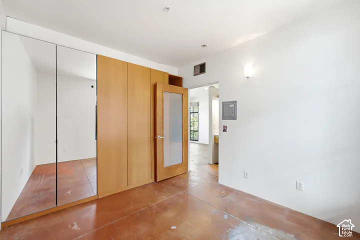 Mirrored sliding closet doors, wood-finish built-in cabinetry, frosted glass paneled door, and polished concrete flooring