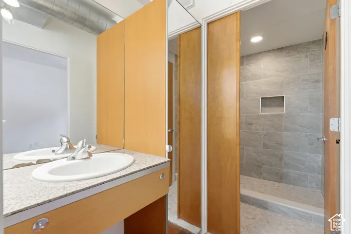 Double vanity with integrated sinks, light-toned countertop, wood-finish cabinetry, and a walk-in shower with tiled walls and a recessed niche