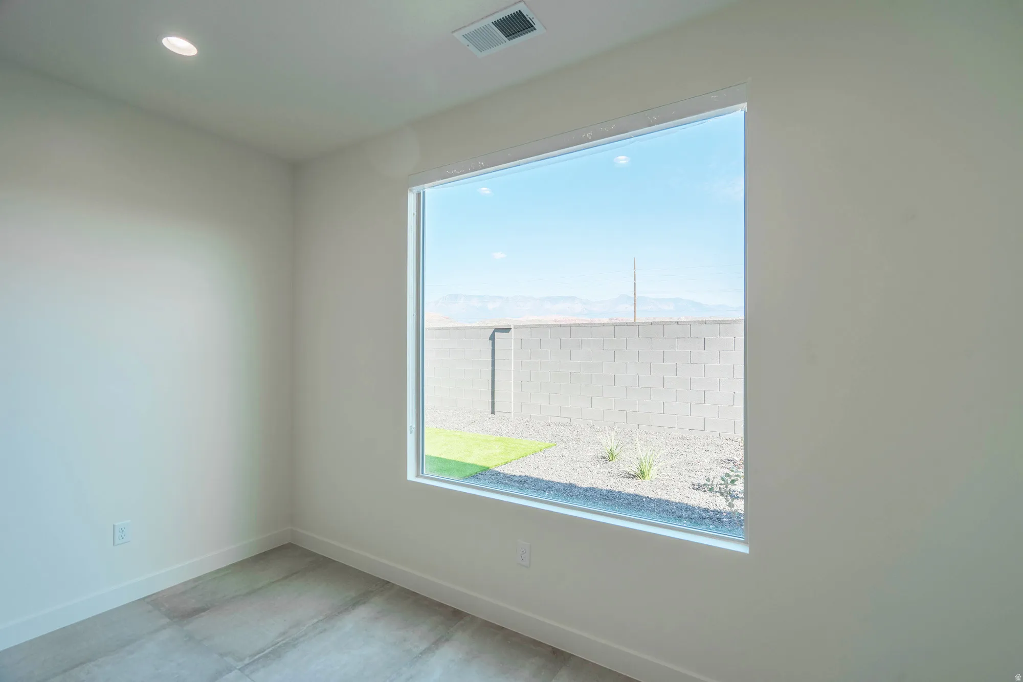 Bright corner bedroom showcasing expansive windows framing outdoor landscape, polished concrete flooring, and recessed ceiling lighting