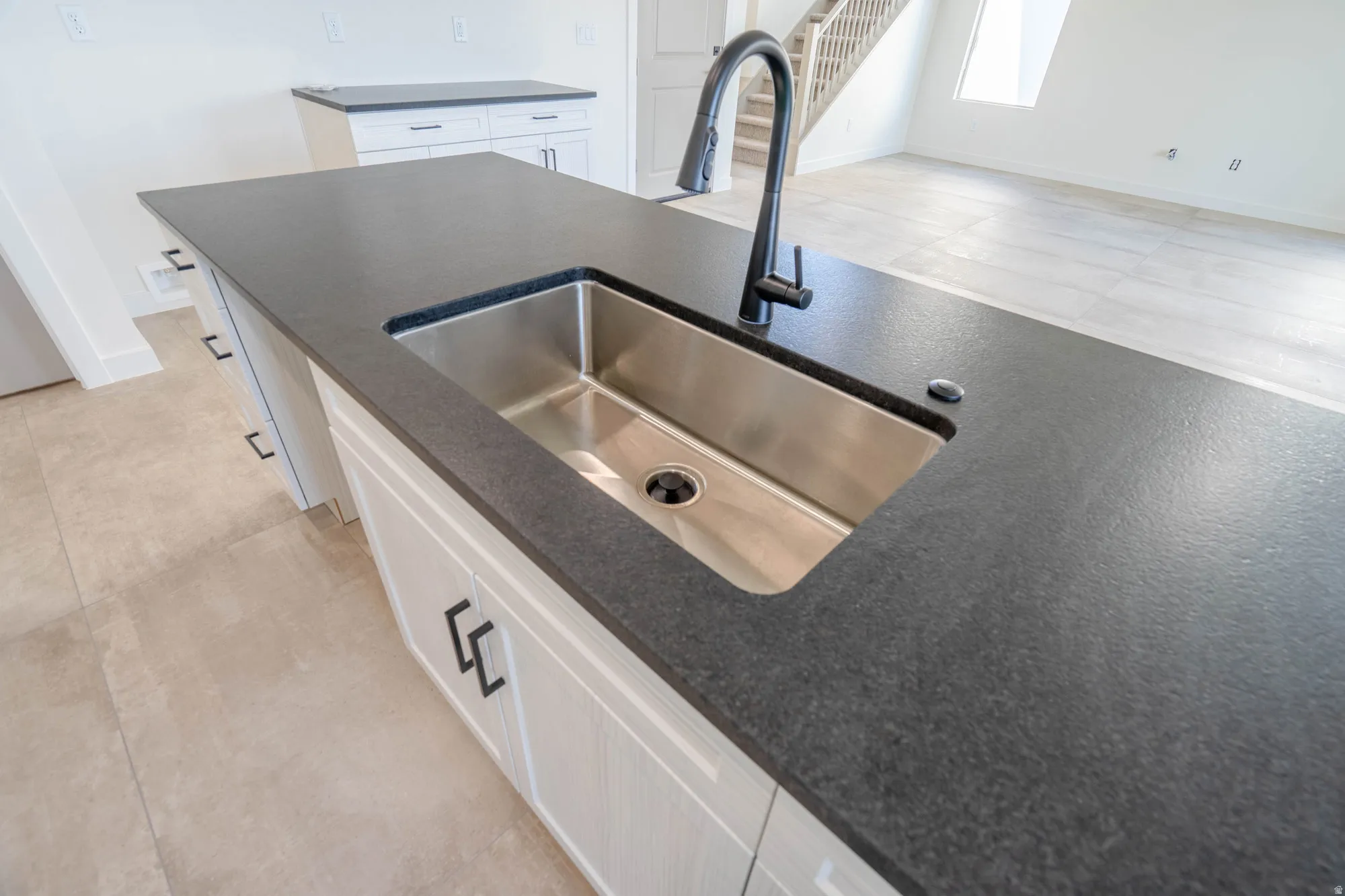 Kitchen island with a stainless steel undermount sink, dark countertop, and matte black faucet