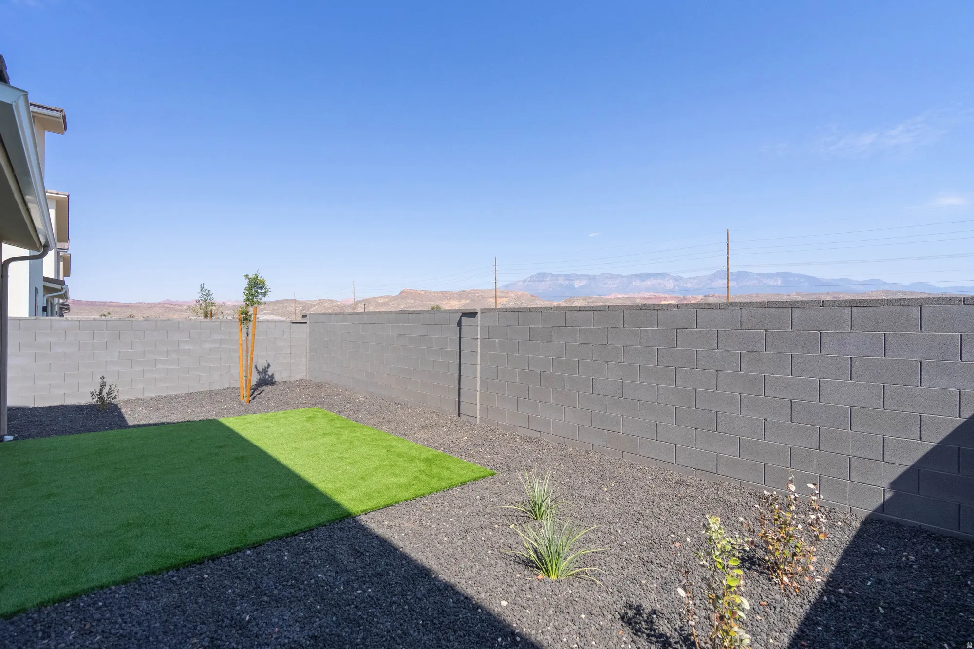 Enclosed backyard featuring a dark gray block wall, a section of artificial turf, and dark gravel landscaping