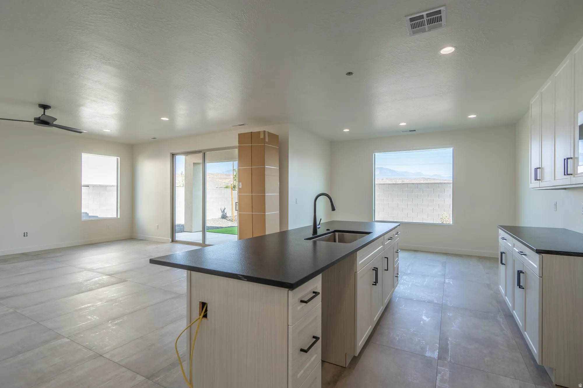 Spacious open-concept area featuring a kitchen island with sink and matte black faucet, recessed lighting, and sliding glass doors to the exterior