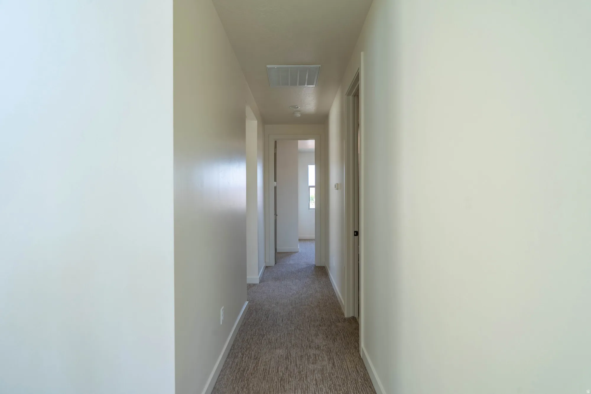 Hallway featuring light-toned walls, carpeted flooring, recessed lighting, and a white door with a dark handle