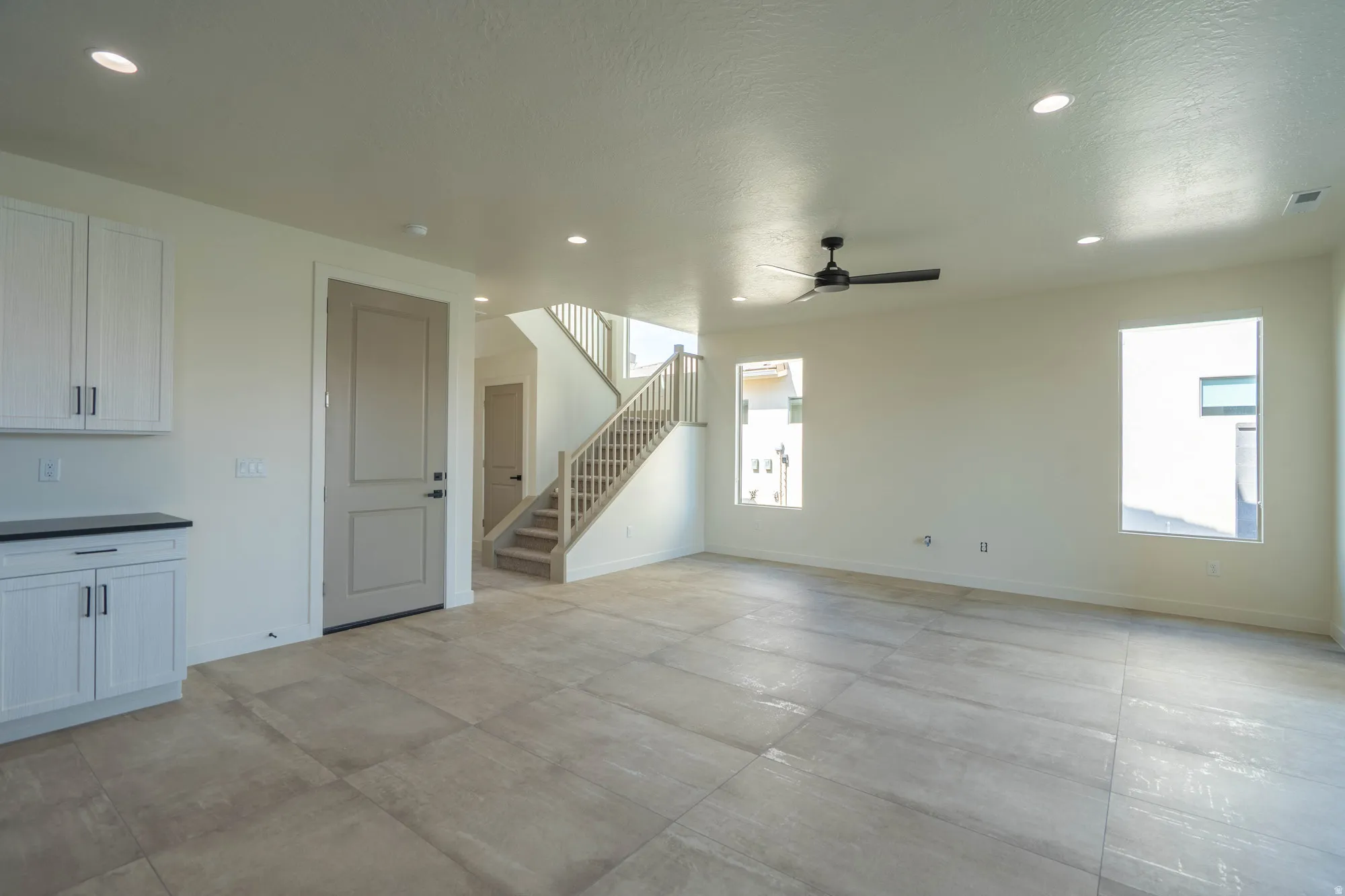 Recessed lighting, ceiling fan, LVT flooring, white cabinetry with black countertops, and a staircase with wood railing
