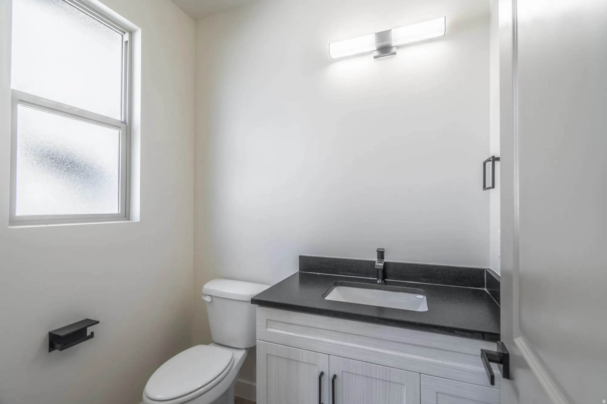 Modern bathroom featuring a white cabinetry vanity with a black countertop and integrated rectangular sink, chrome faucet, and polished nickel hardware