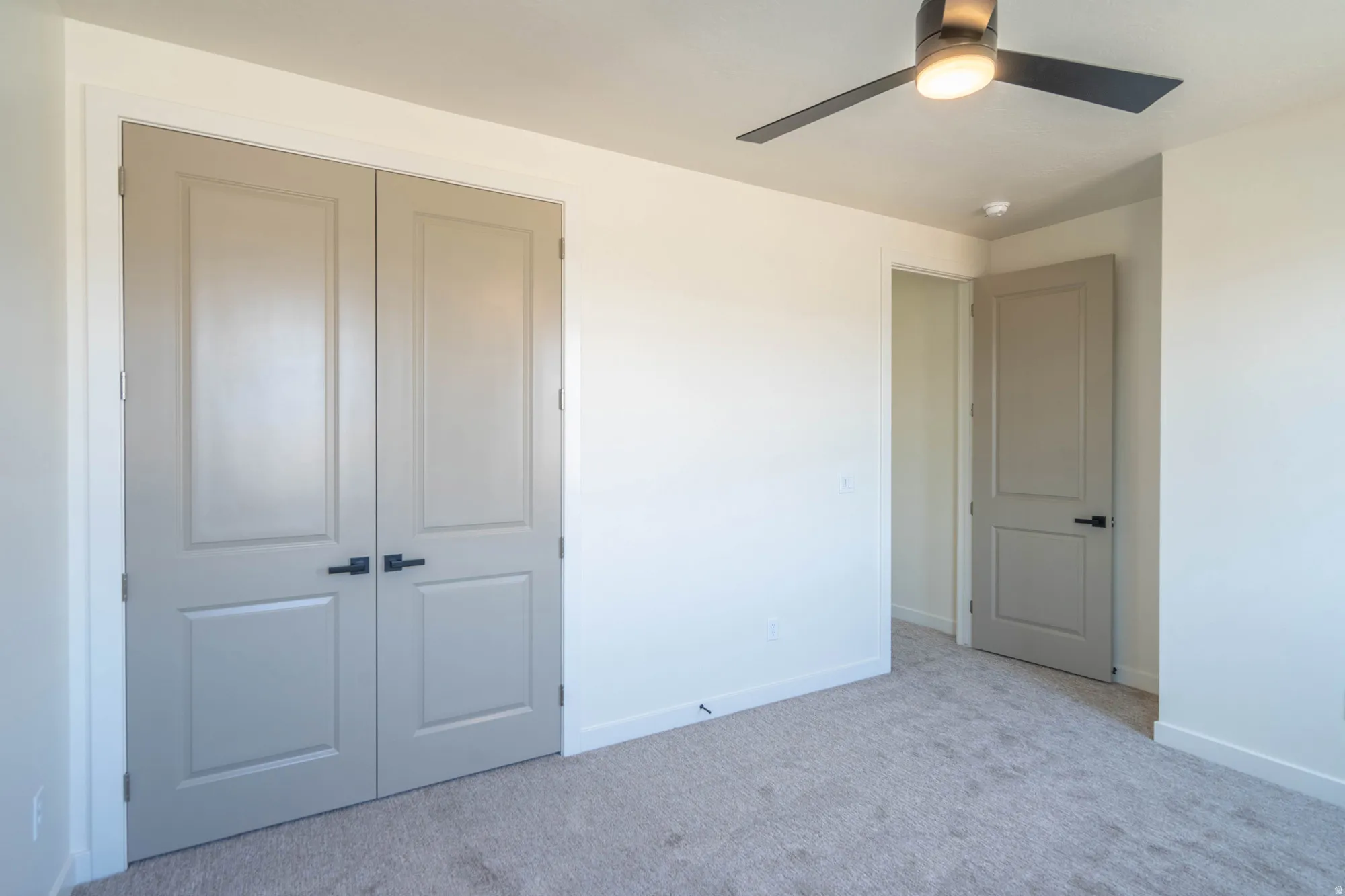 Light-colored carpeting, modern ceiling fan with integrated lighting, flat panel doors with dark hardware, and white wall finishes