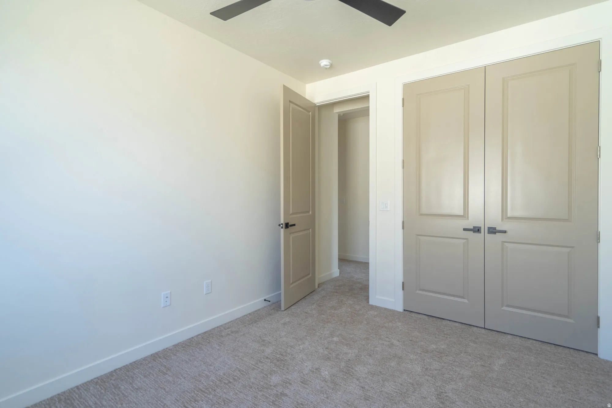 Neutral tone wall color with carpeted flooring, featuring a ceiling fan, light-toned interior doors, and a double-door closet