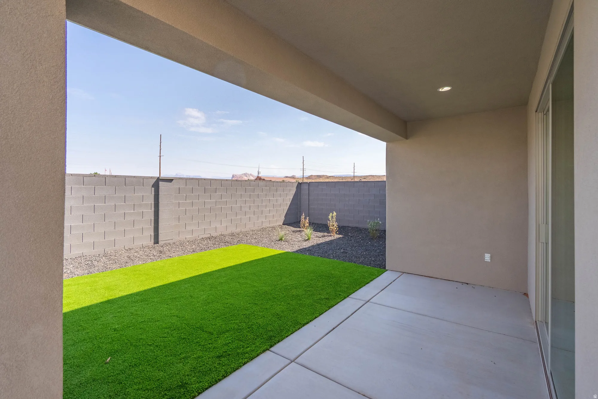 Covered patio area with recessed lighting, concrete flooring, sliding glass door, artificial turf, and block wall perimeter