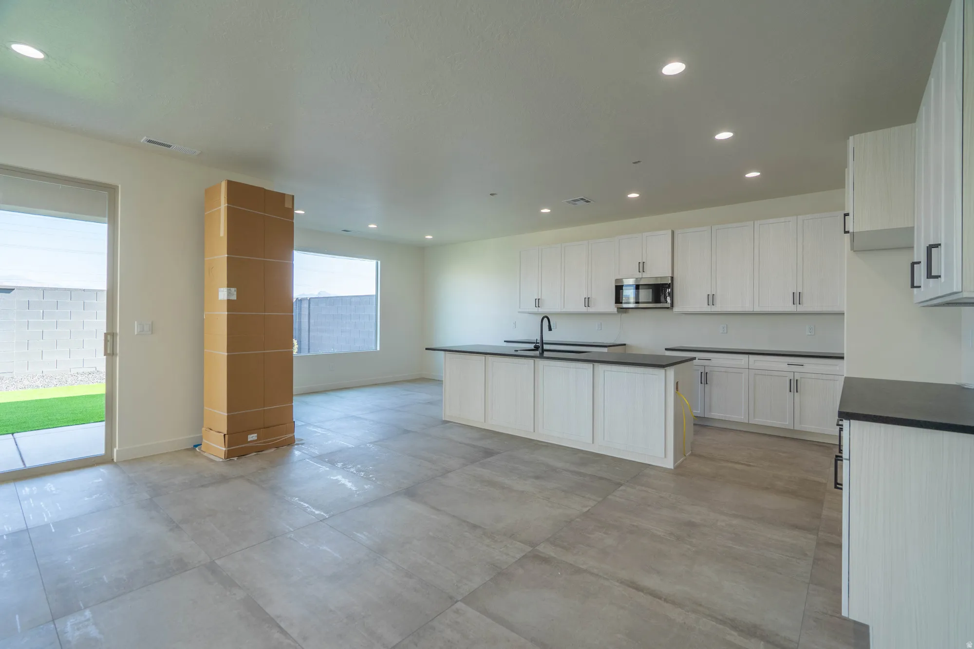 Spacious open-concept living area featuring large format tile flooring, a modern kitchen with white cabinetry, dark countertops, and a built-in microwave
