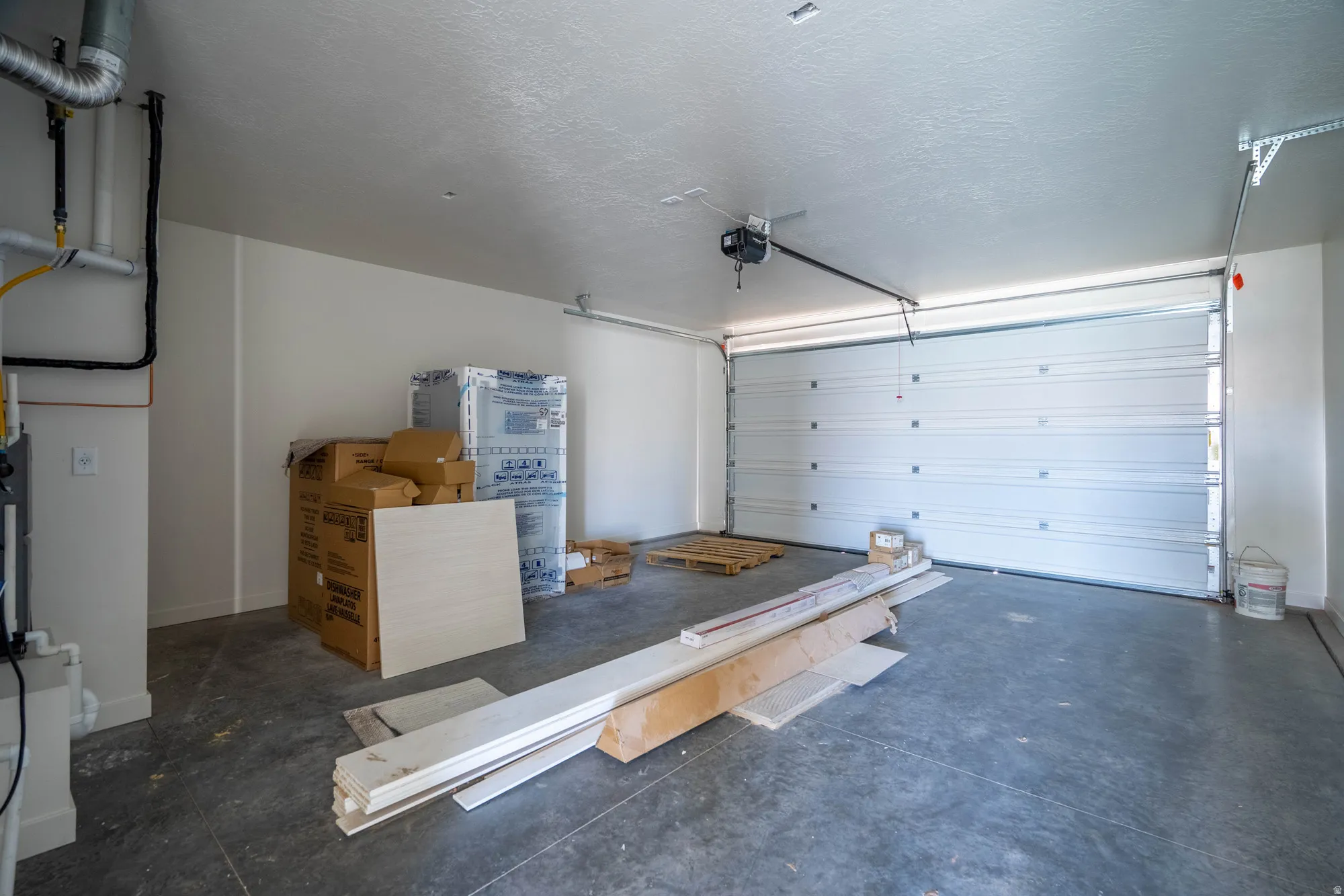 Attached garage featuring a sectional door, concrete flooring, and exposed utility lines