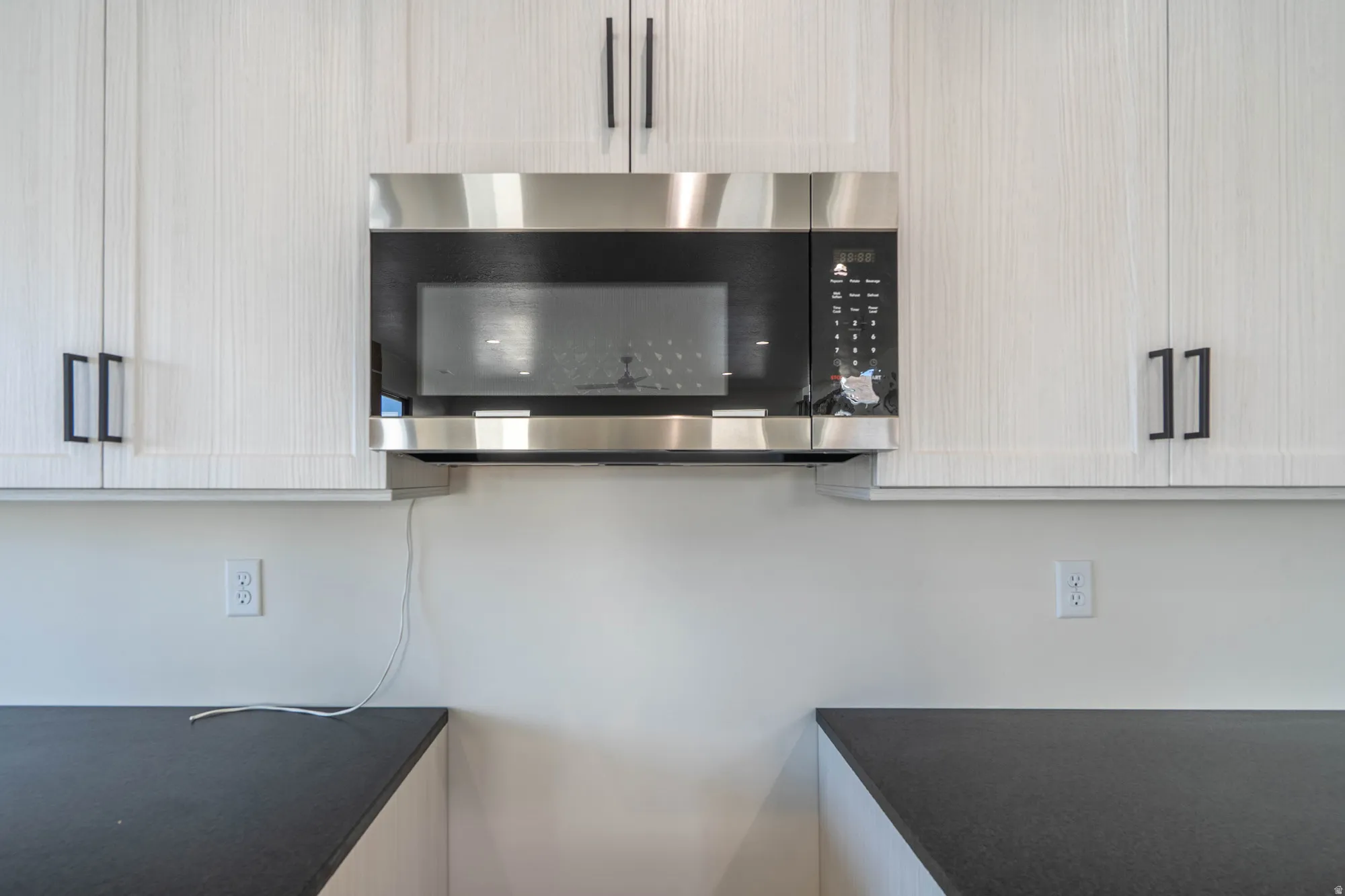 White upper cabinetry with black hardware, stainless steel over-the-range microwave, and dark countertops