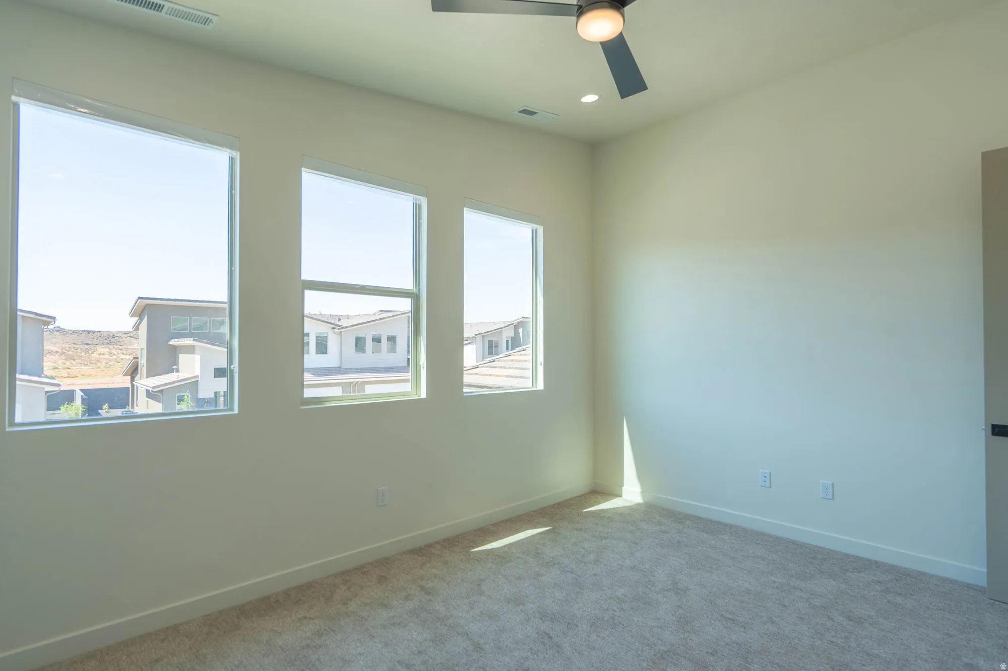 Three large windows, recessed lighting, ceiling fan with light, and plush carpet flooring
