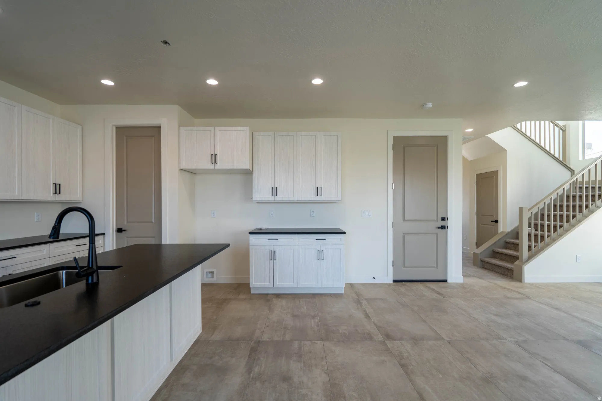 Kitchen island with a dark countertop and undermount sink, white cabinetry with dark hardware, recessed lighting, and wood-look flooring