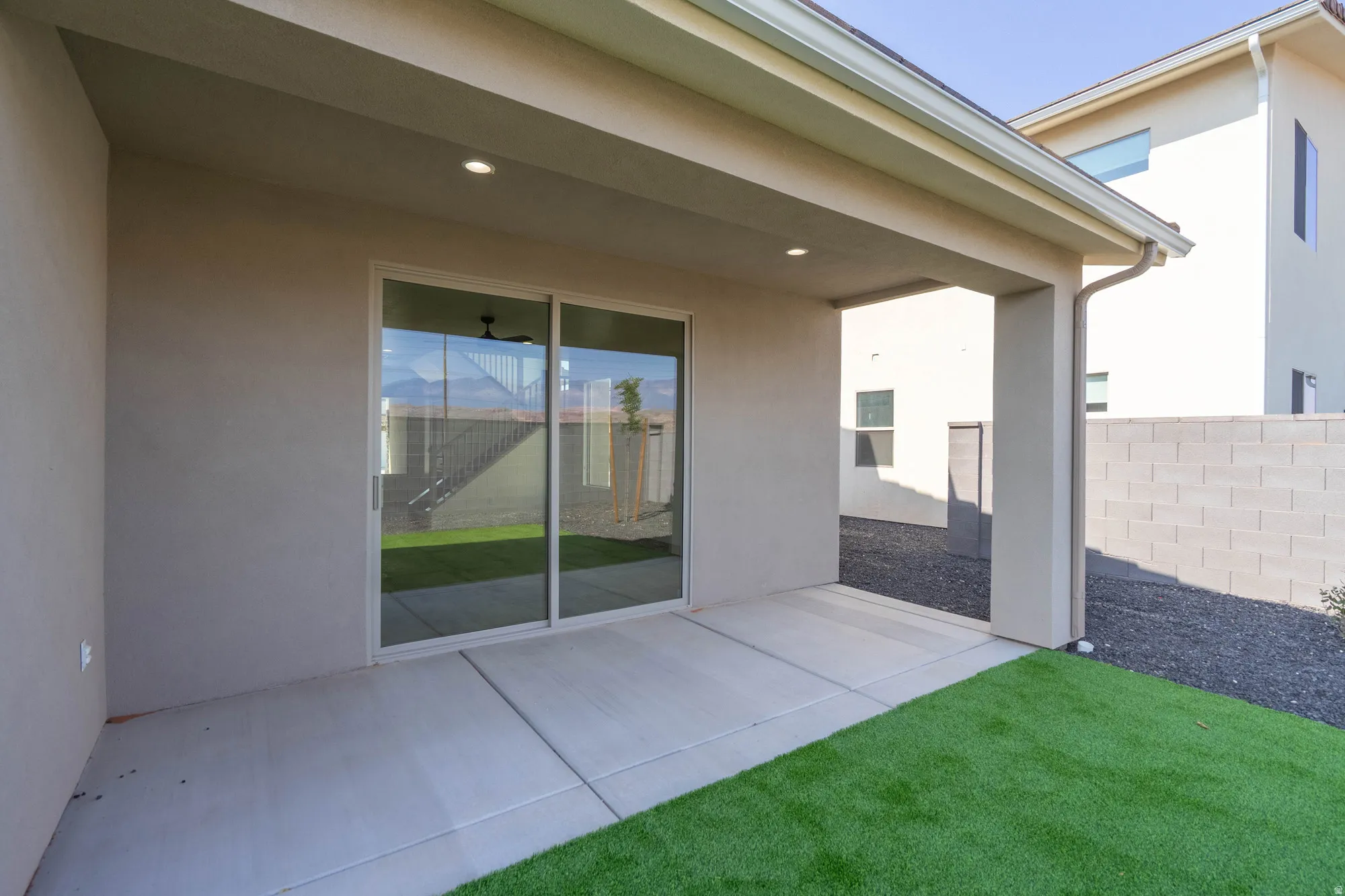 Covered patio with recessed lighting, concrete flooring, sliding glass door, and artificial turf