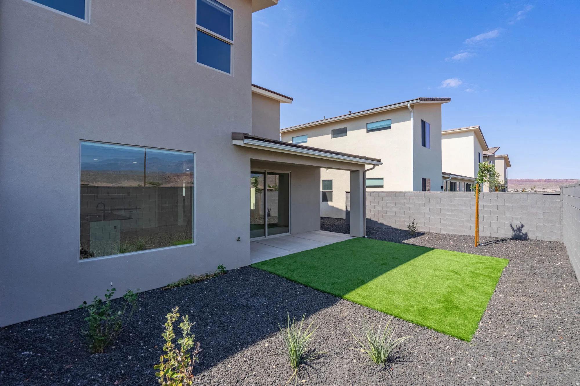 Private backyard featuring a covered patio, artificial turf, and a block wall perimeter