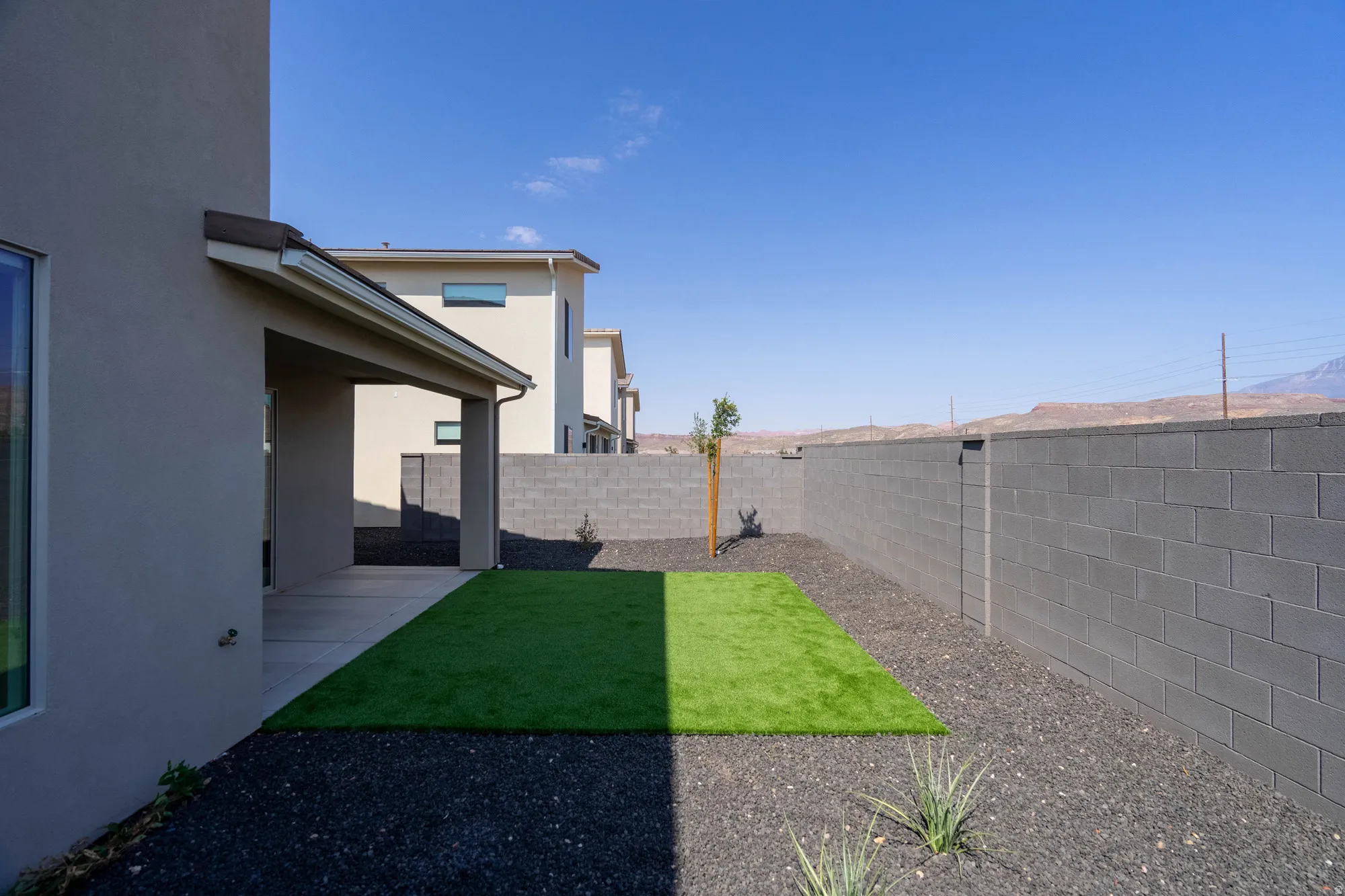 Rear exterior featuring a covered patio, artificial turf, gravel landscaping, and a masonry perimeter wall
