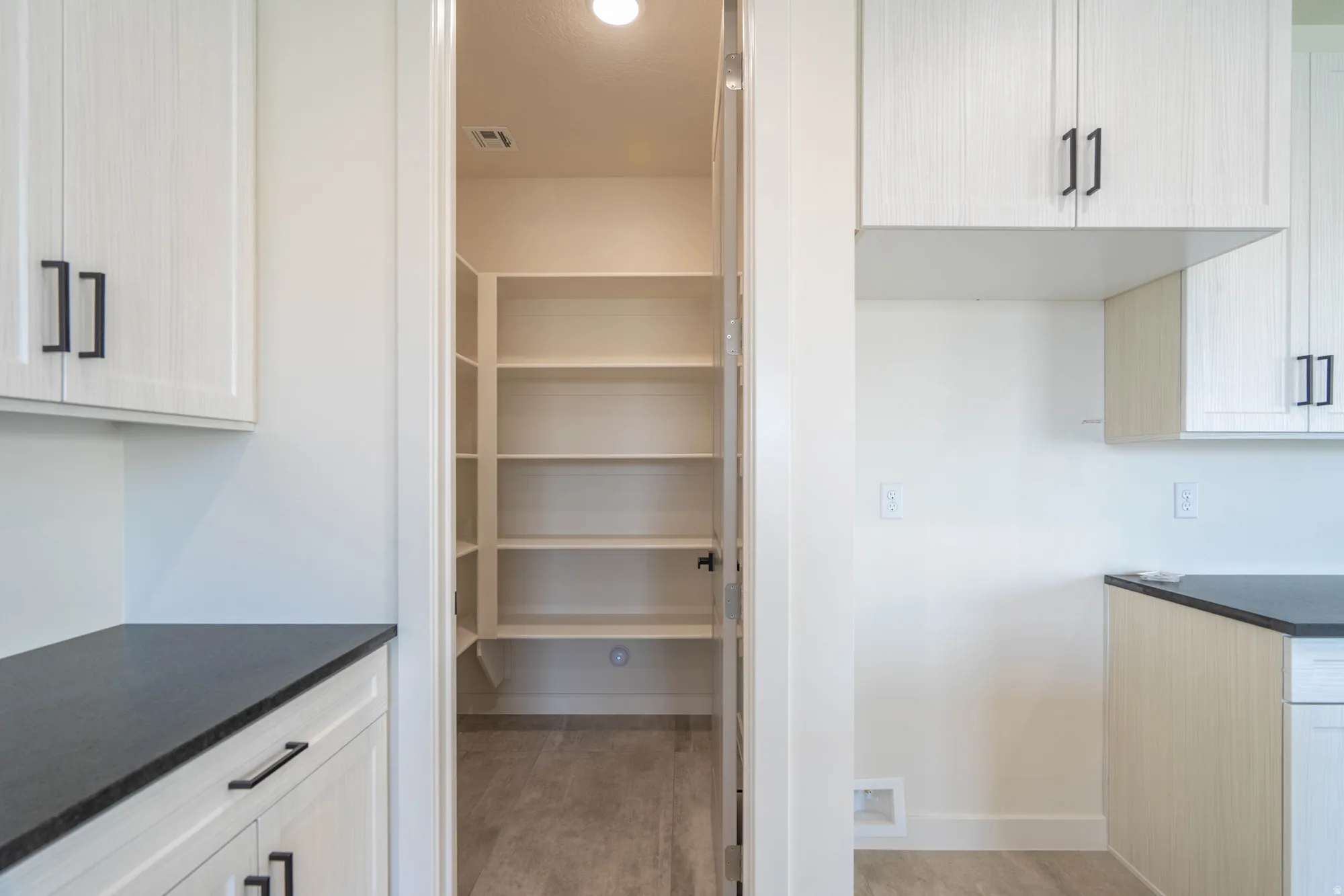 Spacious pantry with built-in shelving, complemented by white cabinetry and dark countertops