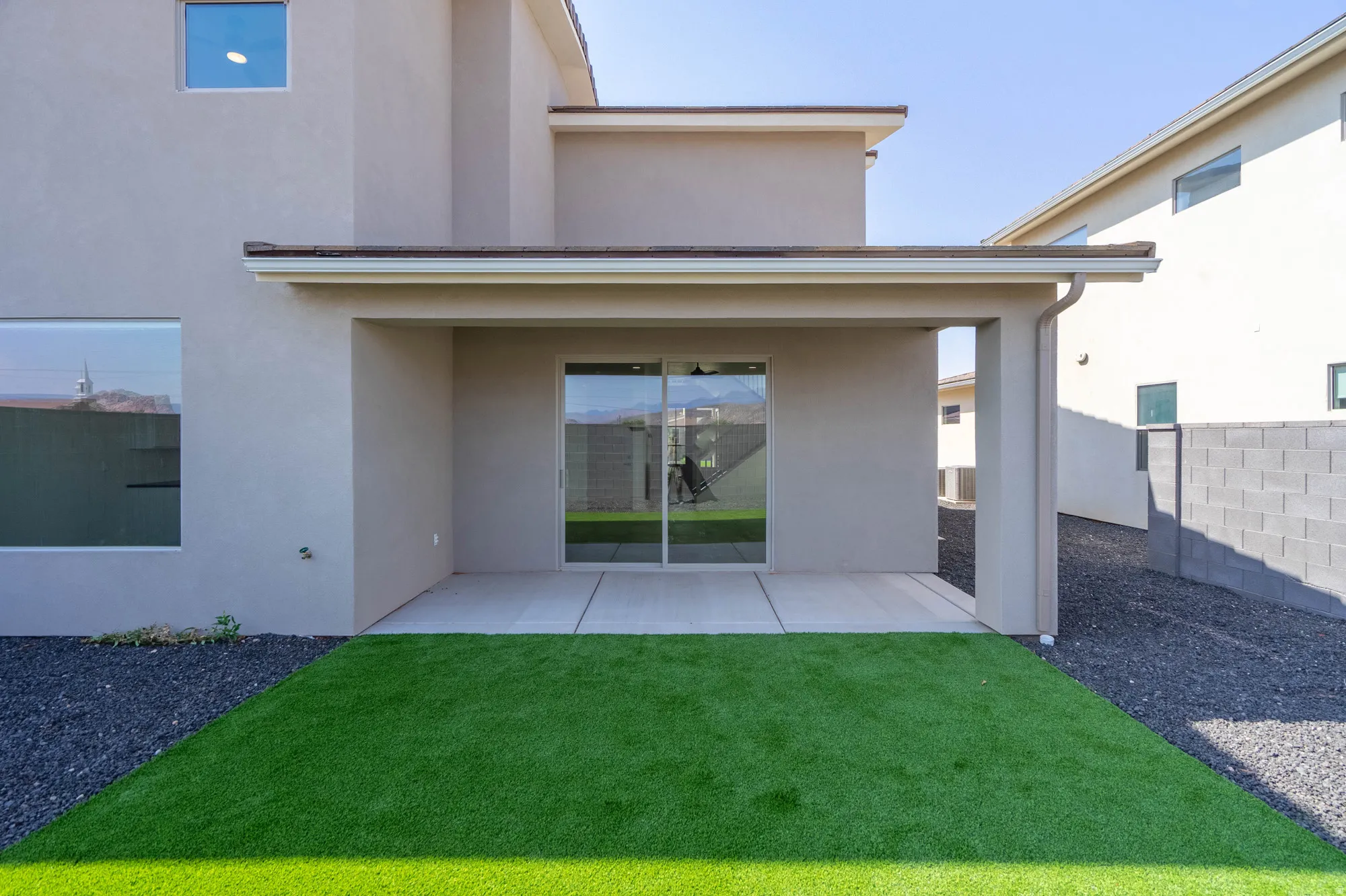 Private backyard featuring a covered patio, sliding glass door access, synthetic turf, and dark gravel landscaping