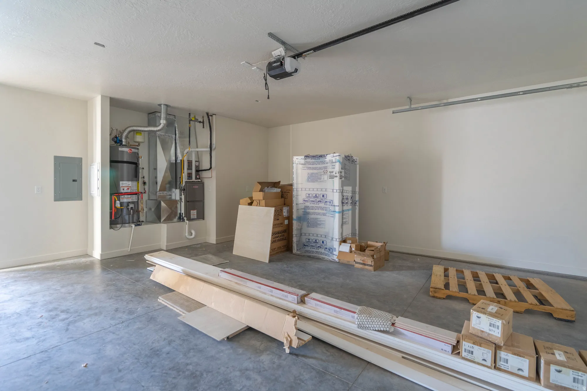Concrete flooring, interior utility closet with water heater, electrical panel, and exposed ceiling-mounted garage door opener