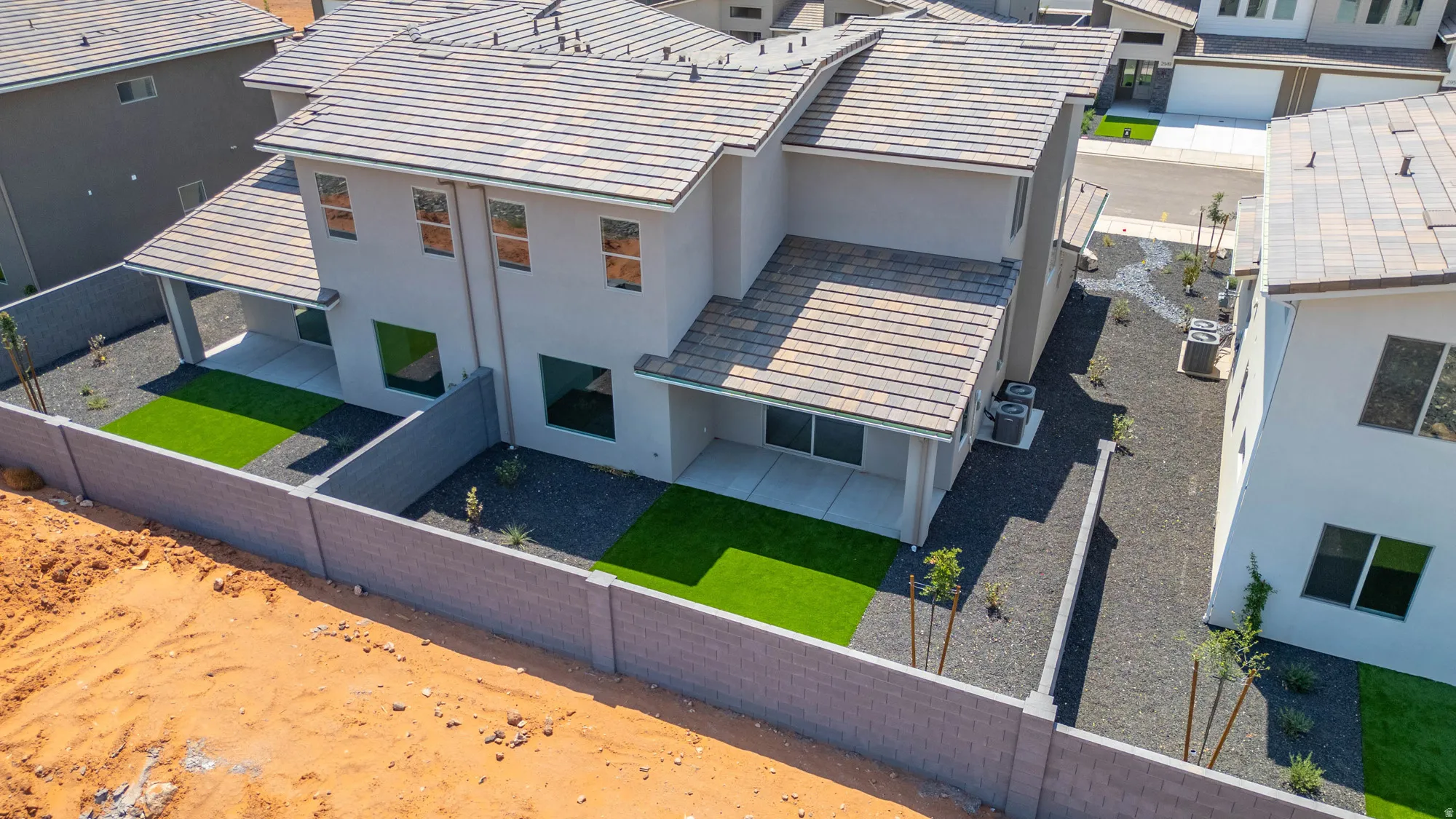 Contemporary stucco exterior with tile roofing, ground-level patios, and artificial turf accents