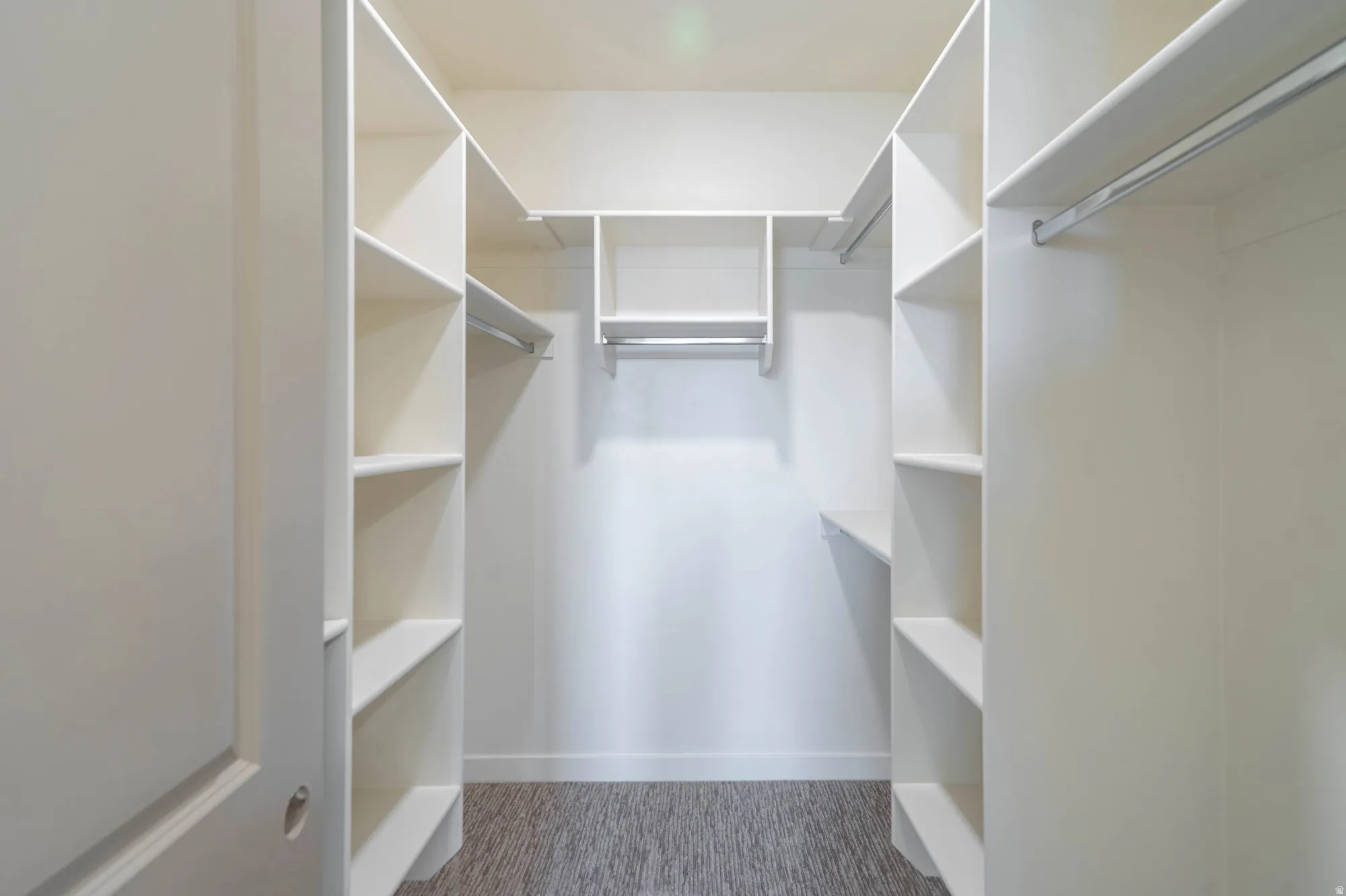 Walk-in closet with integrated shelving units, multiple hanging rods, and wood-finish flooring