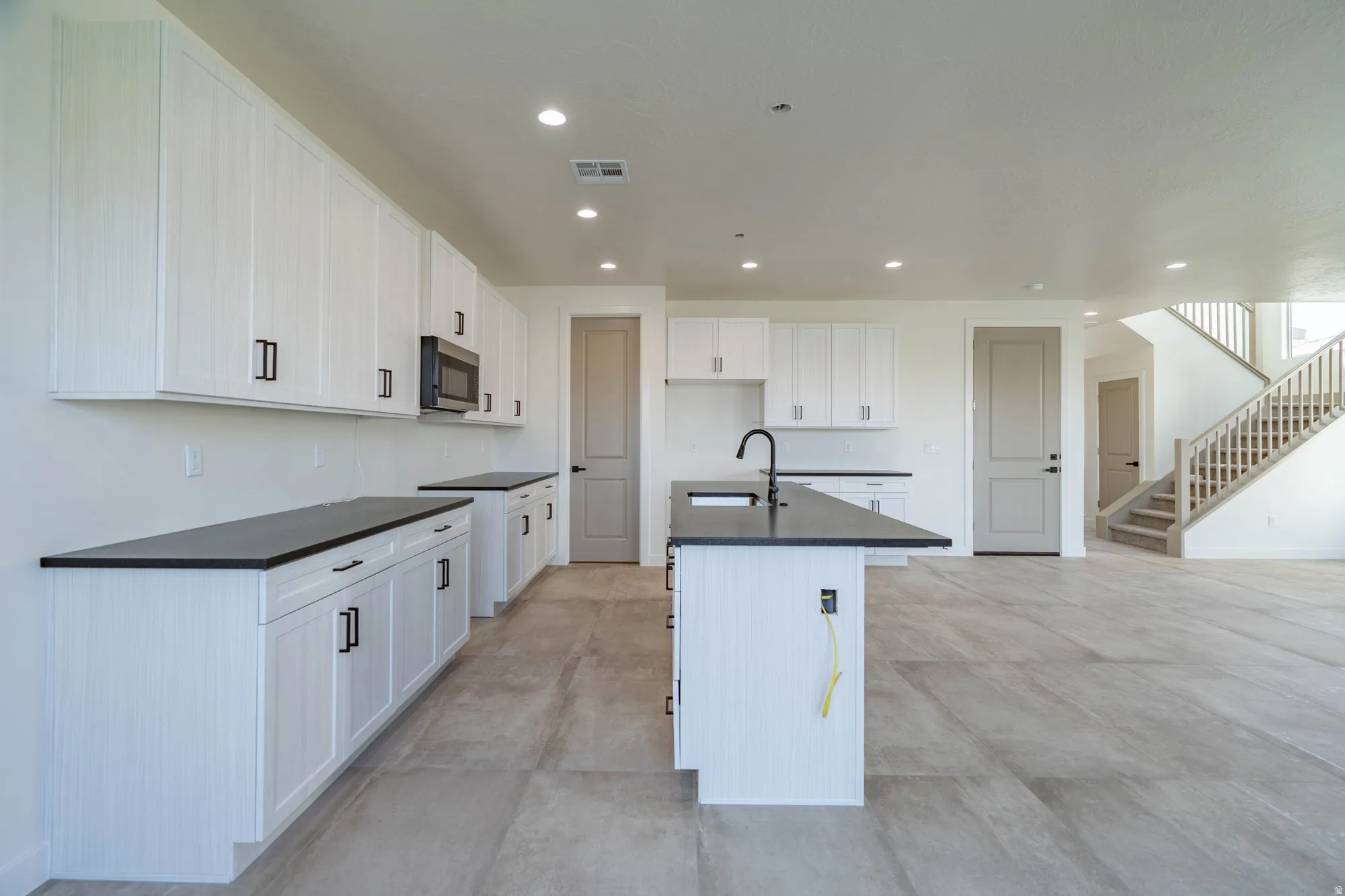 Kitchen featuring white cabinetry, dark countertops, a built-in microwave, and a central island with a sink