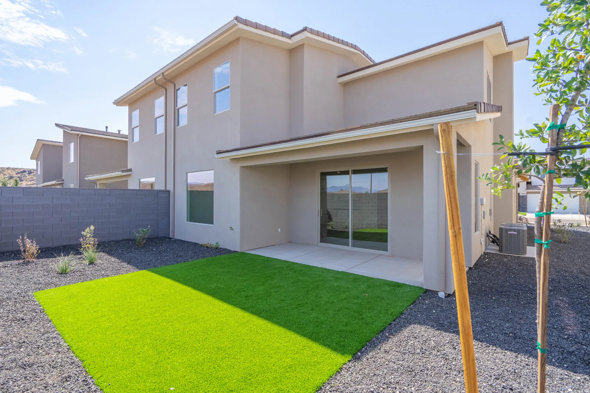 Covered patio with sliding glass doors, artificial turf, and dark gravel landscaping