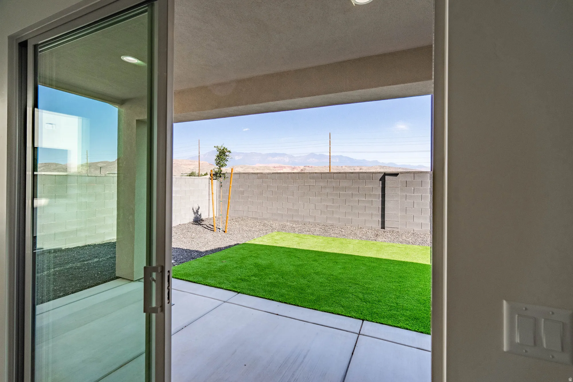 Sliding glass door opening to a concrete patio, artificial turf, and gravel landscaping
